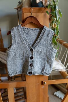 a gray sweater vest sitting on top of a wooden chair