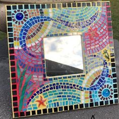 a colorful mosaic mirror sitting on top of a cement slab