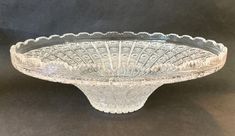 an ornate glass bowl with scalloped edges on a black background in front of a dark backdrop