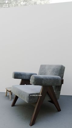 a gray chair sitting on top of a cement floor next to a white wall and wooden legs