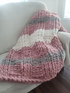 a pink and gray blanket sitting on top of a white couch