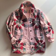 a pink jacket that is sitting on the floor next to a white wall with a red and green patchwork pattern