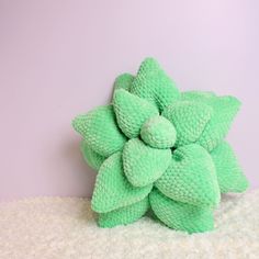 a green stuffed flower sitting on top of a pile of white fluffy material next to a purple wall