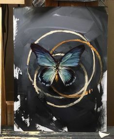 a blue butterfly sitting on top of a black and white painting with gold circles around it