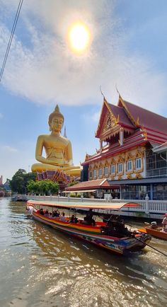 a boat traveling down a river next to a tall building with a giant buddha statue in the background