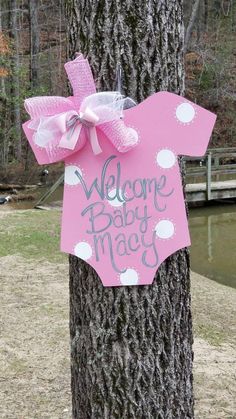 a welcome baby sign is attached to a tree trunk with a pink bow on it