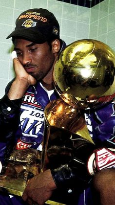 a man sitting down holding two trophies in his hands and looking at the camera with one hand on his face