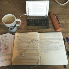 an open book sitting on top of a wooden table next to a laptop computer and cup of coffee