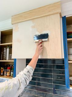 a person with a paint roller painting a kitchen counter top in blue and white tiles