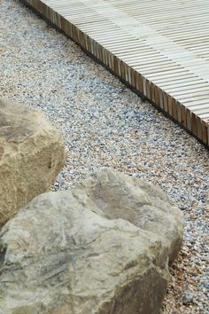 a bird sitting on top of a rock next to a wooden walkway area with rocks and gravel