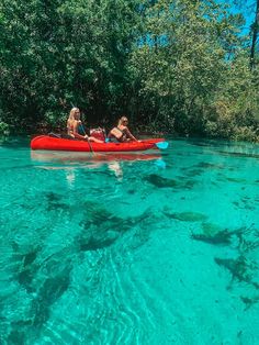 two people in a red canoe paddling through clear blue water