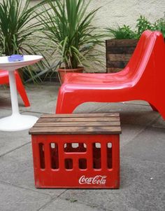 a red plastic chair sitting next to a small table with a coca cola box on it