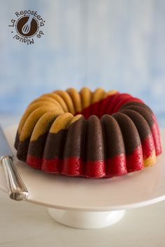 a bundt cake with red, yellow and brown icing on a white plate