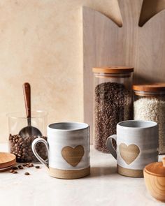 two coffee mugs sitting on top of a counter next to spices and spoons