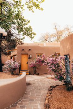 an adobe style house with pink flowers in the front yard and walkway leading up to it