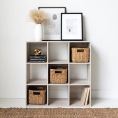 a white shelf with baskets and pictures on it next to a rug in front of a wall