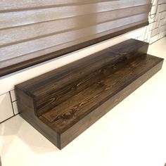 a wooden shelf sitting on top of a white tile counter next to a window with blinds