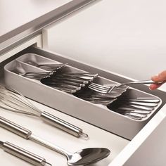 a person holding a fork and spoon in an open drawer with utensils on it