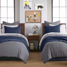 two twin beds with blue and grey comforters in a bedroom area next to windows