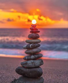 a stack of rocks sitting on top of a beach next to the ocean at sunset