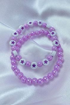 two bracelets with purple beads and white stars on the end are laying on a white sheet