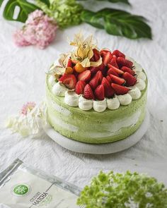 a green cake with strawberries on top sitting on a table next to some flowers