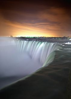 the niagara falls at night with lights in the background and water rushing over it's sides