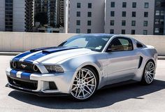 a silver and blue mustang car parked in a parking lot next to a tall building