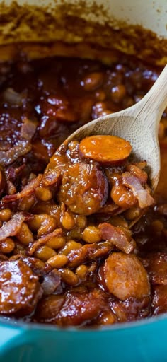 a spoon full of beans and sausage in a blue pot with a wooden spoon sticking out of it