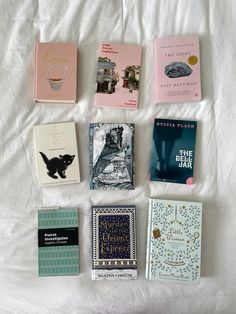 there are many different books on the bed with white sheets in this photo, all lined up together