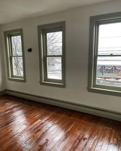 an empty room with three windows and hard wood flooring on one side, looking out onto the street