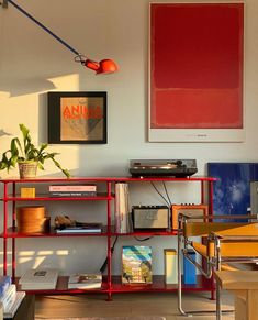 a living room with a red book shelf and pictures on the wall above it,