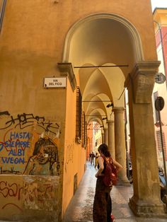 a woman is walking down an alley way with graffiti on the walls and archways