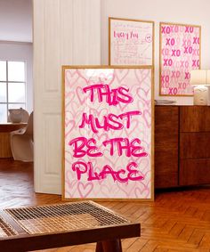 this must be the place sign in front of a wooden table with pink writing on it