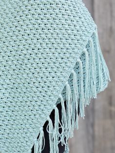 a crocheted shawl with fringes on top of it, against a wooden background