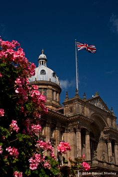 the british flag is flying on top of an old building with pink flowers in front