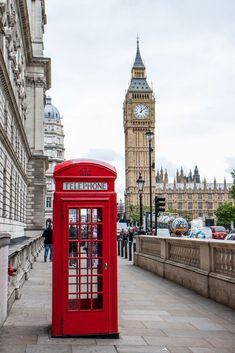 a red phone booth sitting on the side of a road next to a clock tower