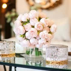 a glass table topped with vases filled with pink flowers next to two crystal cups