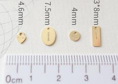 three small gold charms sitting next to a ruler