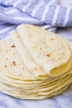 a stack of tortillas sitting on top of a white marble counter next to a blue towel