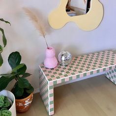 a pink vase sitting on top of a wooden bench next to a mirror and potted plant