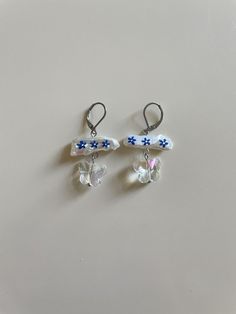 two small white and blue flowers are hanging from hooks on a gray surface with silver earwires