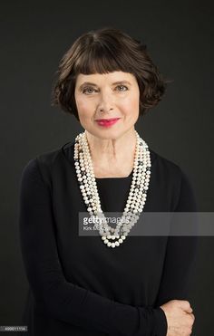 an older woman wearing pearls and a black dress with her arms crossed, looking at the camera