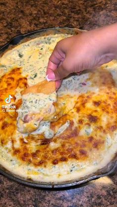 a person dipping cheese onto a pizza in a pan on top of a countertop