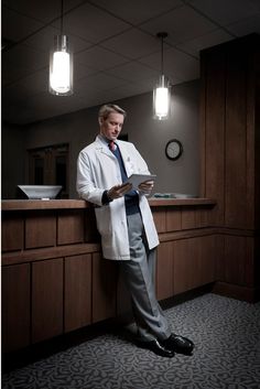 a man in a lab coat standing at a counter looking at something on his tablet