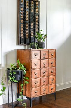 a wooden cabinet with many drawers and plants on top