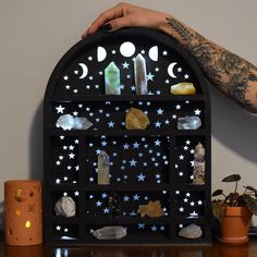 a person holding up a shelf with rocks, crystals and candles on top of it