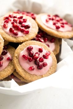 some cookies with pink icing and pomegranates in a white bowl