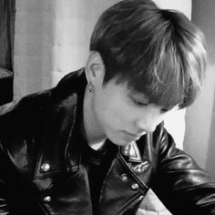 black and white photo of boy in leather jacket looking at his cell phone while sitting down