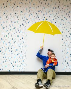 a man sitting on the floor with a child under an umbrella in front of a wall